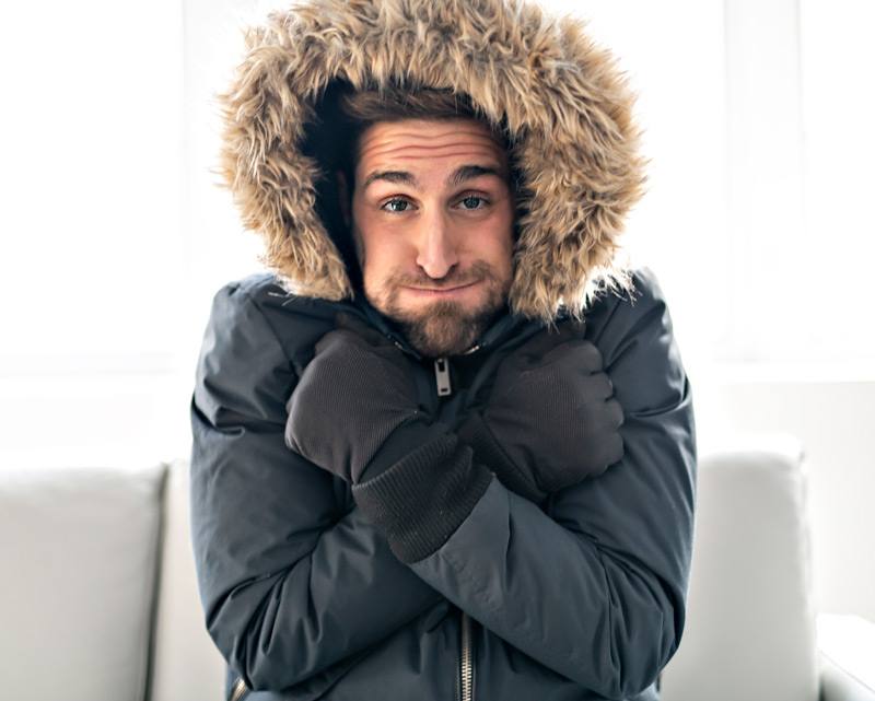 Man in a large coat freezing in his house